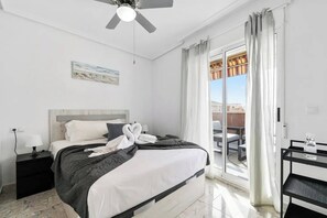 A hotel room with a bed, a nightstand, a desk, a ceiling fan, and a view of the outside. - Penthouse in Central Torrevieja (Torrevieja)