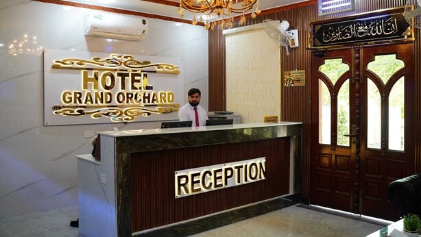 A hotel reception area with a reception desk, a chandelier, a wall-mounted air conditioner, and a wooden door with a window. - Hotel Grand Orchard (Lahore)