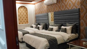 A hotel room with two beds, a mirror, a small table, and patterned wallpaper. - Hotel Grand Orchard (Lahore)