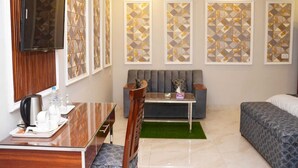 A hotel room with a sofa, a bed, a TV, a table with a tray of breakfast items, and decorative wall panels. - Hotel Grand Orchard (Lahore)