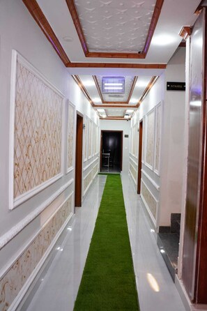 A hallway with a green carpet, white walls, and a sign indicating the location of the stairs.