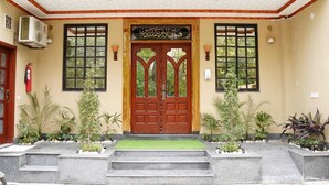 A building with a central wooden door, two windows on either side, and a fire extinguisher mounted on the wall. - Hotel Grand Orchard (Lahore)