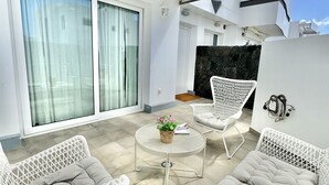Un área exterior moderna con mobiliario de mimbre blanco, una mesa redonda y una pared de piedra.
