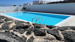 Una piscina bajo un cielo azul despejado, edificios blancos y rocas volcánicas.