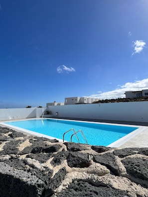 Ein Schwimmbecken mit blauem Himmel, weißen Gebäuden und vulkanischen Felsen.