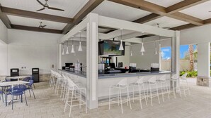 A modern bar area with white bar stools, a counter with a TV, and ceiling fans. - 7 miles to Disney, private pool + lazy river (Kissimmee)