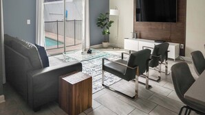 A modern living room with a sofa, chairs, a coffee table, a TV, and a pool view. - 7 miles to Disney, private pool + lazy river (Kissimmee)