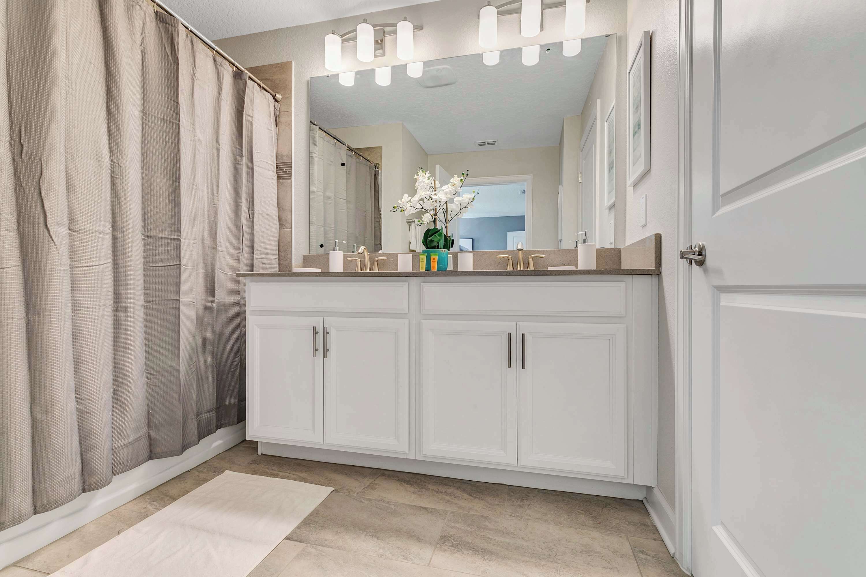 A modern bathroom with a large vanity, a shower curtain, and a mirror with lights.