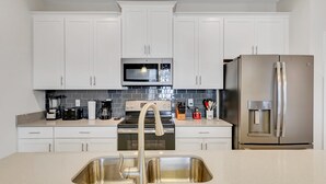 A modern kitchen with white cabinets, a stainless steel sink, a microwave, a stove, and a refrigerator. - 7 miles to Disney, private pool + lazy river (Kissimmee)