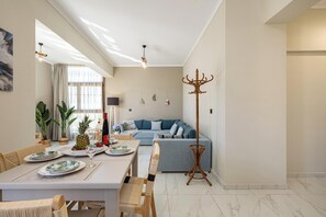 A dining area with a table set for two, a blue sofa, and a floor lamp. - Golden Coast Residences (Vamvakopoulo)