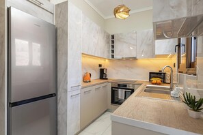 A modern kitchen with a stainless steel refrigerator, a built-in oven, and a coffee maker. - Golden Coast Residences (Vamvakopoulo)