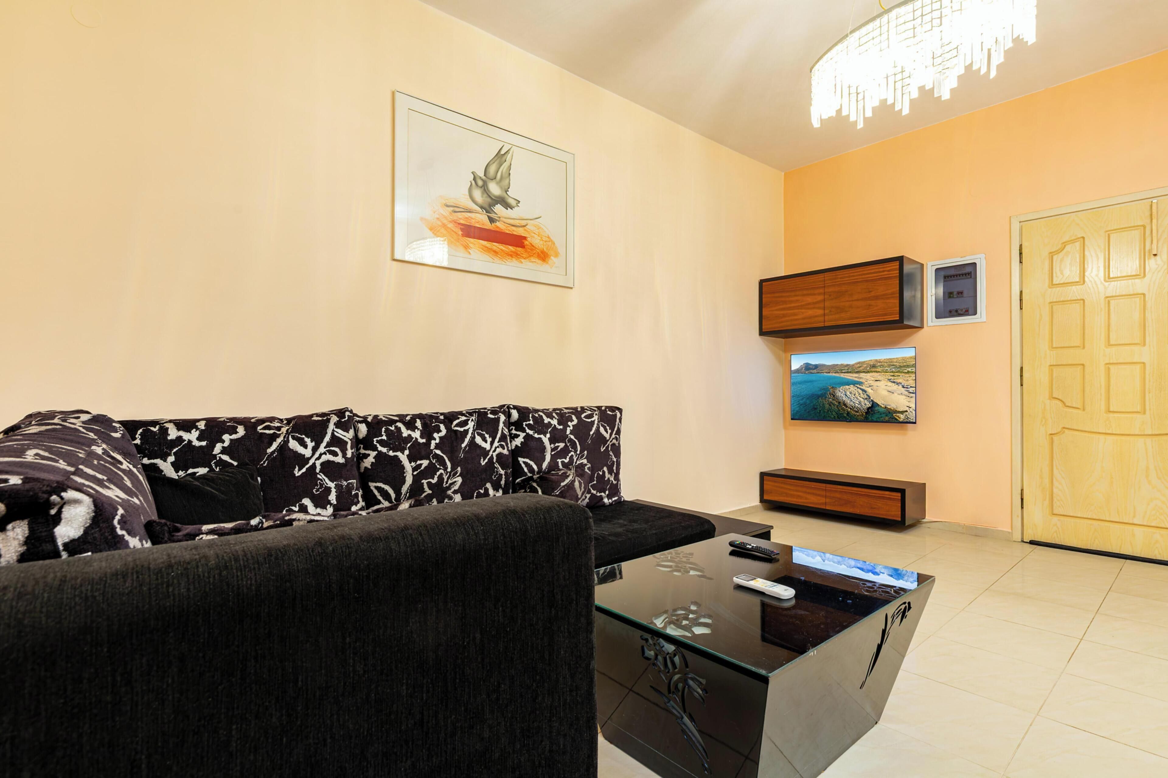 A living room with a sofa, a coffee table, a painting, a television, and a door.