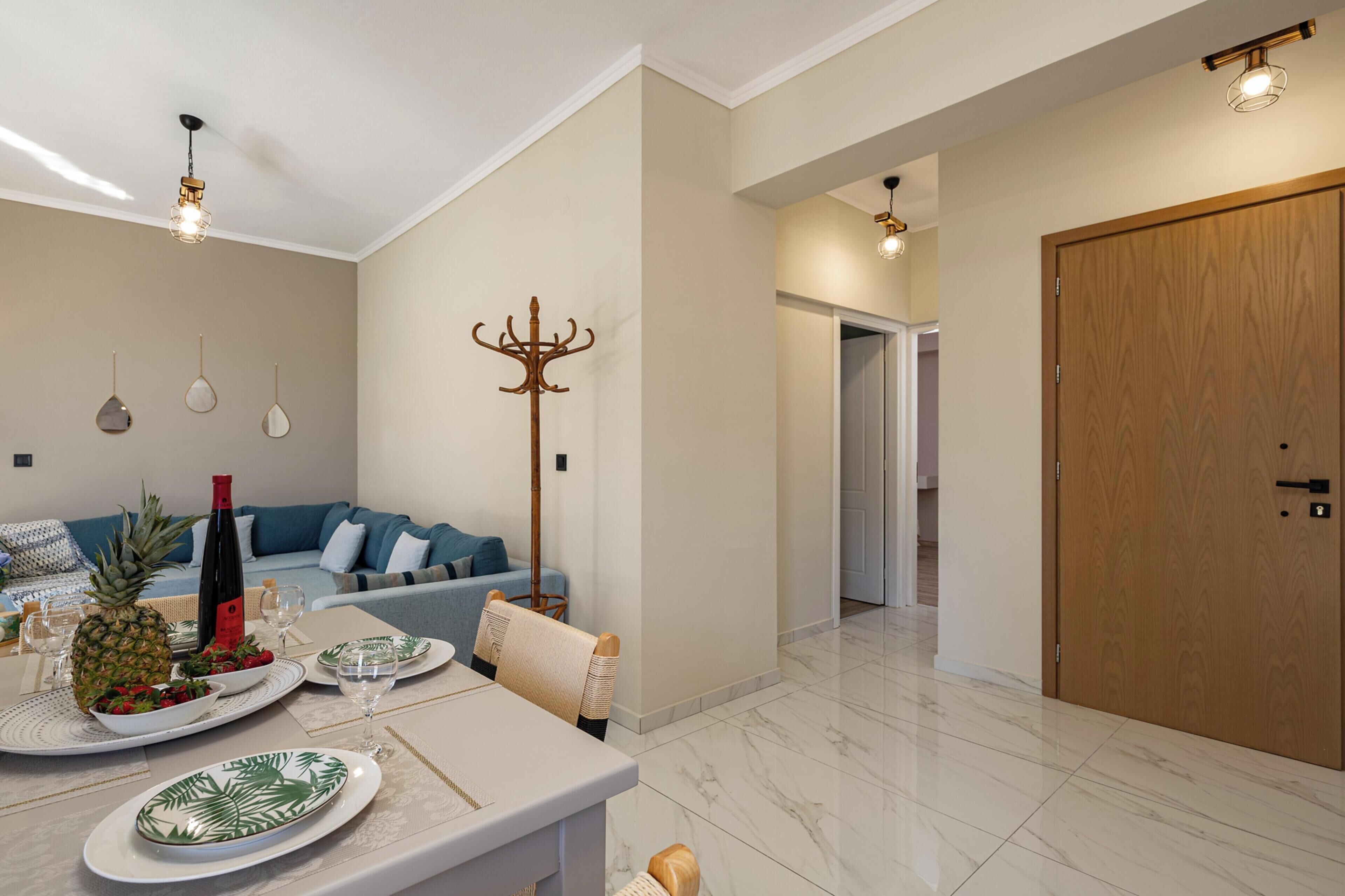 A modern living room with a sofa, a dining table set with plates and glasses, a coat rack, and a wooden door.