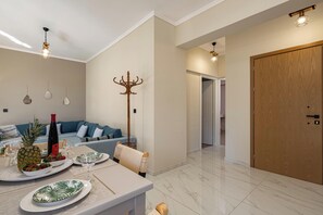 A modern living room with a sofa, a dining table set with plates and glasses, a coat rack, and a wooden door. - Golden Coast Residences (Vamvakopoulo)