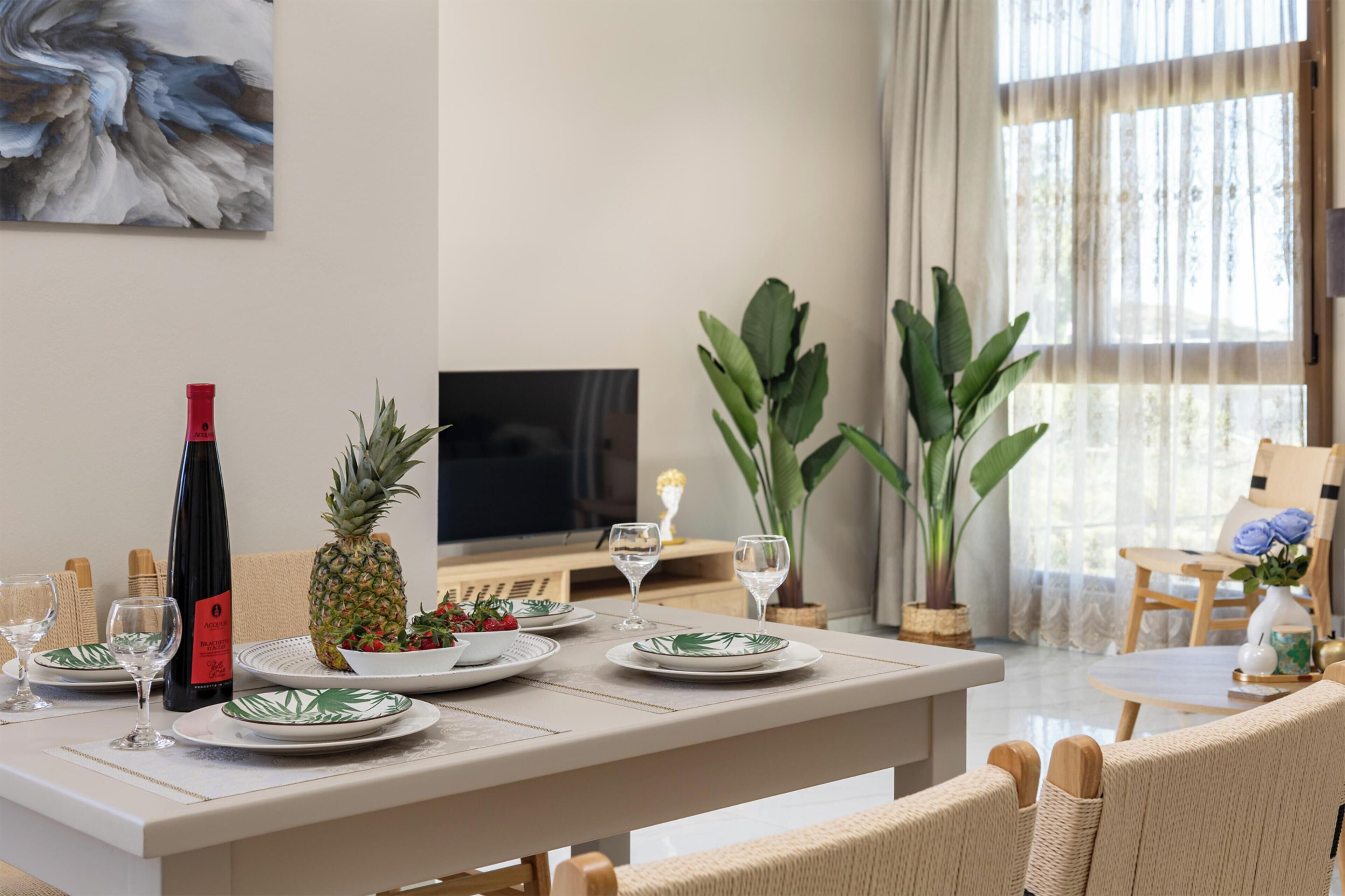 A dining area with a table set for two, a bottle of wine, and a pineapple.