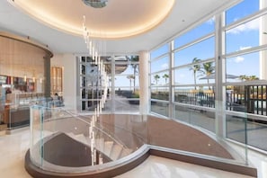 A spacious atrium with a glass railing, a central light fixture, and a view of the outdoors. - Elevated Coastal Escape | Luxury 2BR Amrit Resort (Riviera Beach)