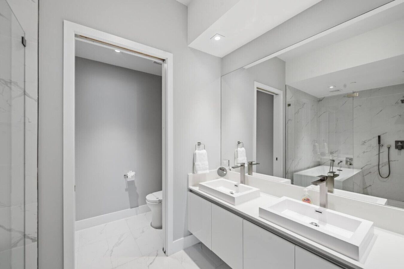 Un baño moderno con un espejo grande, tres lavamanos y una zona de ducha.