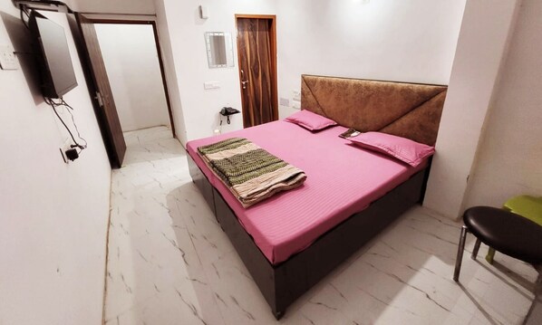 A bedroom with a bed, a chair, a TV, a mirror, and a door. - Hotel JK (Hanumangarh)