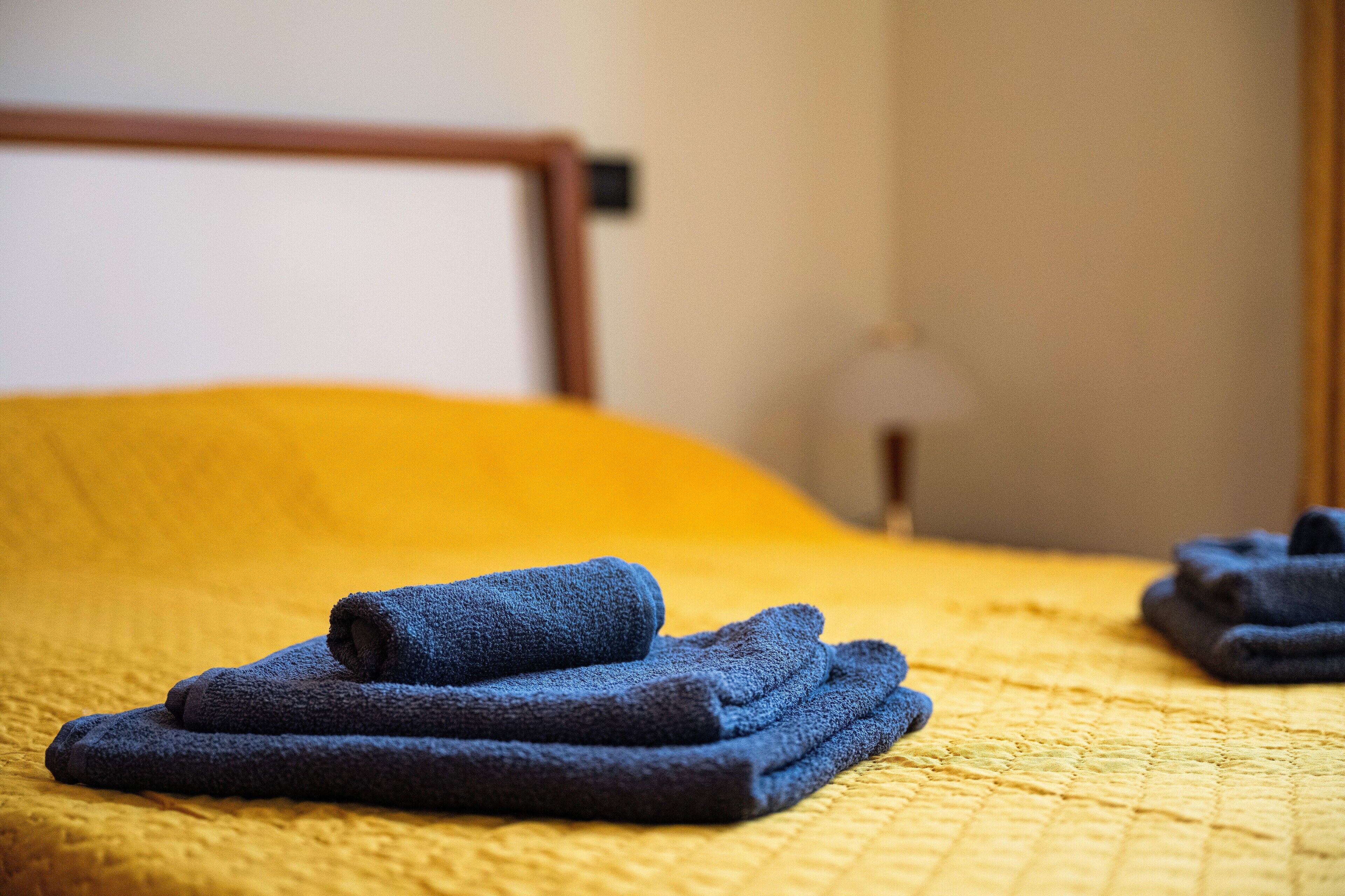 A bed with a yellow quilt and folded dark blue towels.