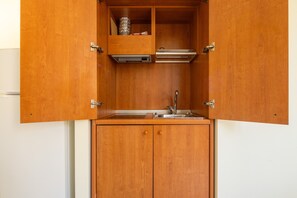 Une cuisine compacte dotée d’un évier encastré, d’un petit plan de travail et d’un meuble avec une porte à charnières.