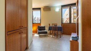 A room with a dining table, chairs, a cabinet, and a window with an air conditioner. - Accommodation with Private Parking - Cagliari (Cagliari)