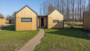 Un edificio moderno in legno con una porta centrale, circondato da un'area verde e alberi.