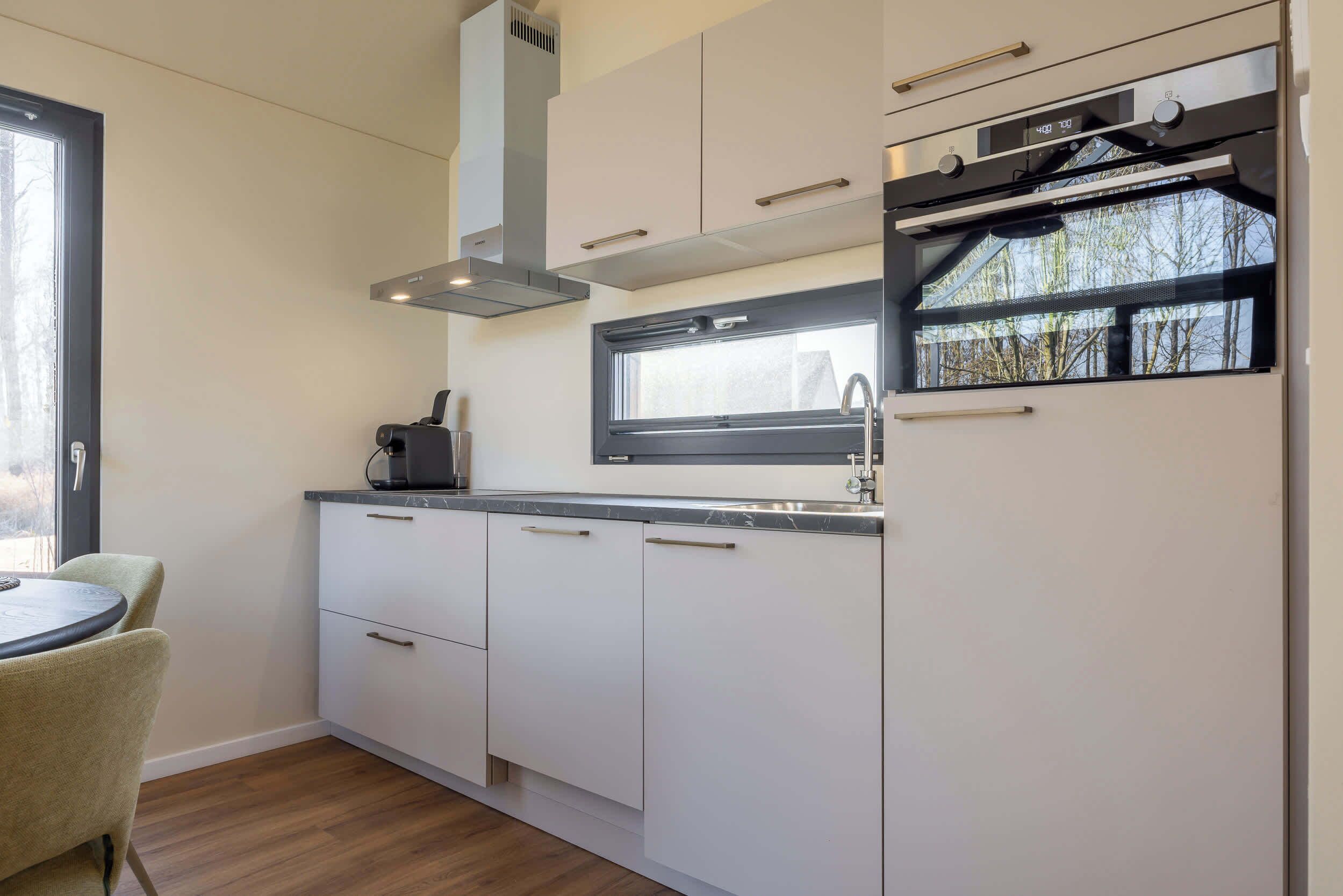 Een moderne keuken met witte kasten, een raam en een inbouwoven.
