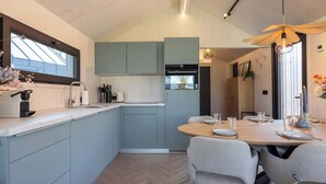 Una cocina moderna con armarios azul claro, una zona de comedor con una mesa de madera y sillas grises, y un ventilador de techo.