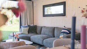 Una sala de estar moderna con un sofá seccional gris, una pequeña mesa redonda y una ventana con vista a follaje.