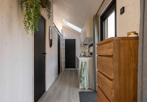 A narrow hallway with a kitchen area, a wooden cabinet, and a hanging plant.