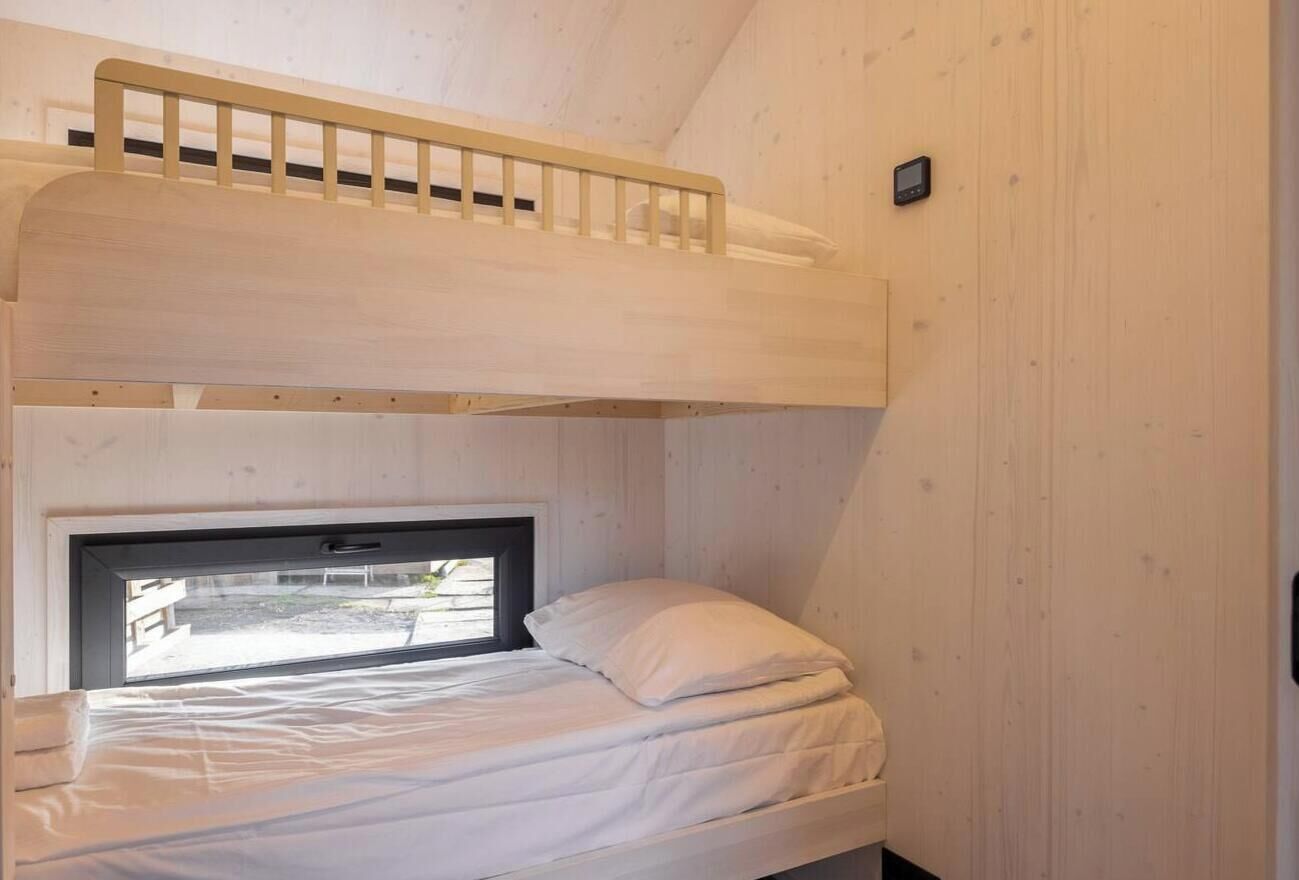 A bunk bed with a window, wooden walls, and a small device on the wall.