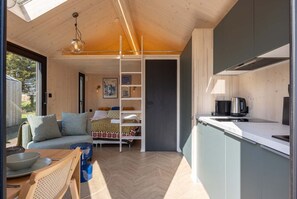 A compact living space with a kitchenette, a sofa, a dining area, and a loft bedroom with a skylight.