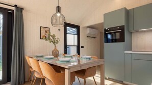 A modern kitchen with a built-in oven, a dining area with a wooden table and chairs, and a pendant light. - Tiny House with forest view in Oud Ade | Tuin van Keet - 27 (Oud Ade)
