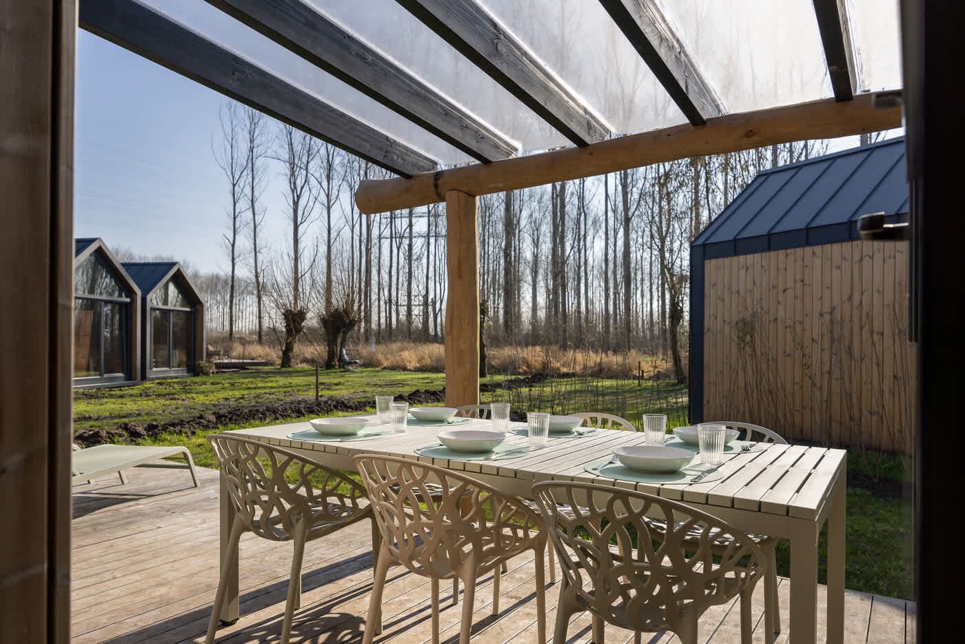Een buiten eetgedeelte met een houten pergola, een gedekte tafel voor vier personen en stoelen.