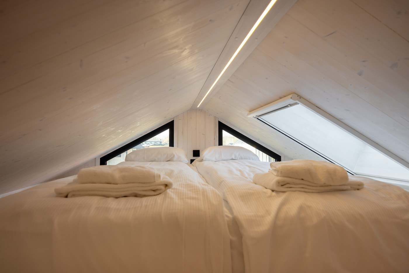 Une chambre avec deux lits, une lucarne et un plafond en bois.