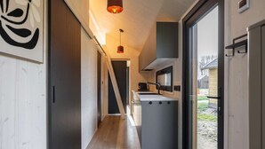 A narrow hallway leading to a kitchen with a large window, a door, and a staircase. - Tiny House with air conditioning in Oud Ade | Tuin van Keet - 17 (Oud Ade)