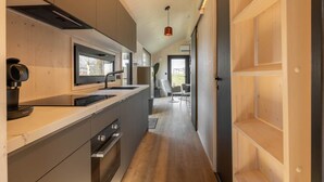 A modern kitchen with a built-in island, a coffee machine, and a view into the dining area. - Tiny House with air conditioning in Oud Ade | Tuin van Keet - 17 (Oud Ade)