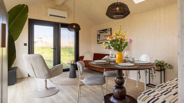 A modern interior with a dining area, a large plant, and a view through a glass door. - Tiny House with air conditioning in Oud Ade | Tuin van Keet - 17 (Oud Ade)