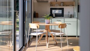 Une cuisine moderne avec un coin repas, une plante en pot et une vue à travers une porte vitrée.