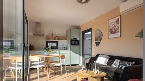 Un salon moderne comprenant un canapé, une table à manger avec des chaises, un coin cuisine avec des placards et des appareils électroménagers, et une grande fenêtre.