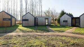 Une rangée de cabanes en bois, reliées par un sentier de terre, et entourées d’arbres.