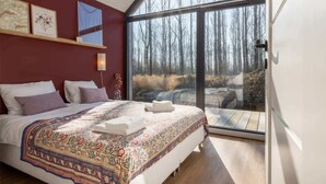 Une chambre avec un grand lit, une fenêtre donnant sur la forêt et un plancher en bois.