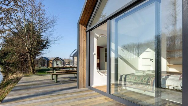 Un bâtiment moderne doté de grandes portes vitrées, d’une terrasse en bois et offrant une vue sur les environs.