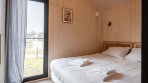 Une chambre à coucher avec un lit, une fenêtre avec des rideaux, un tableau au mur et une vue sur l’extérieur.