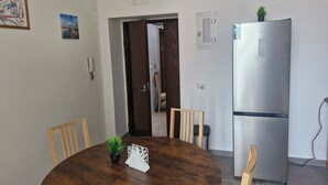 Un comedor con una mesa redonda de madera, sillas, una pequeña planta en maceta y un refrigerador.