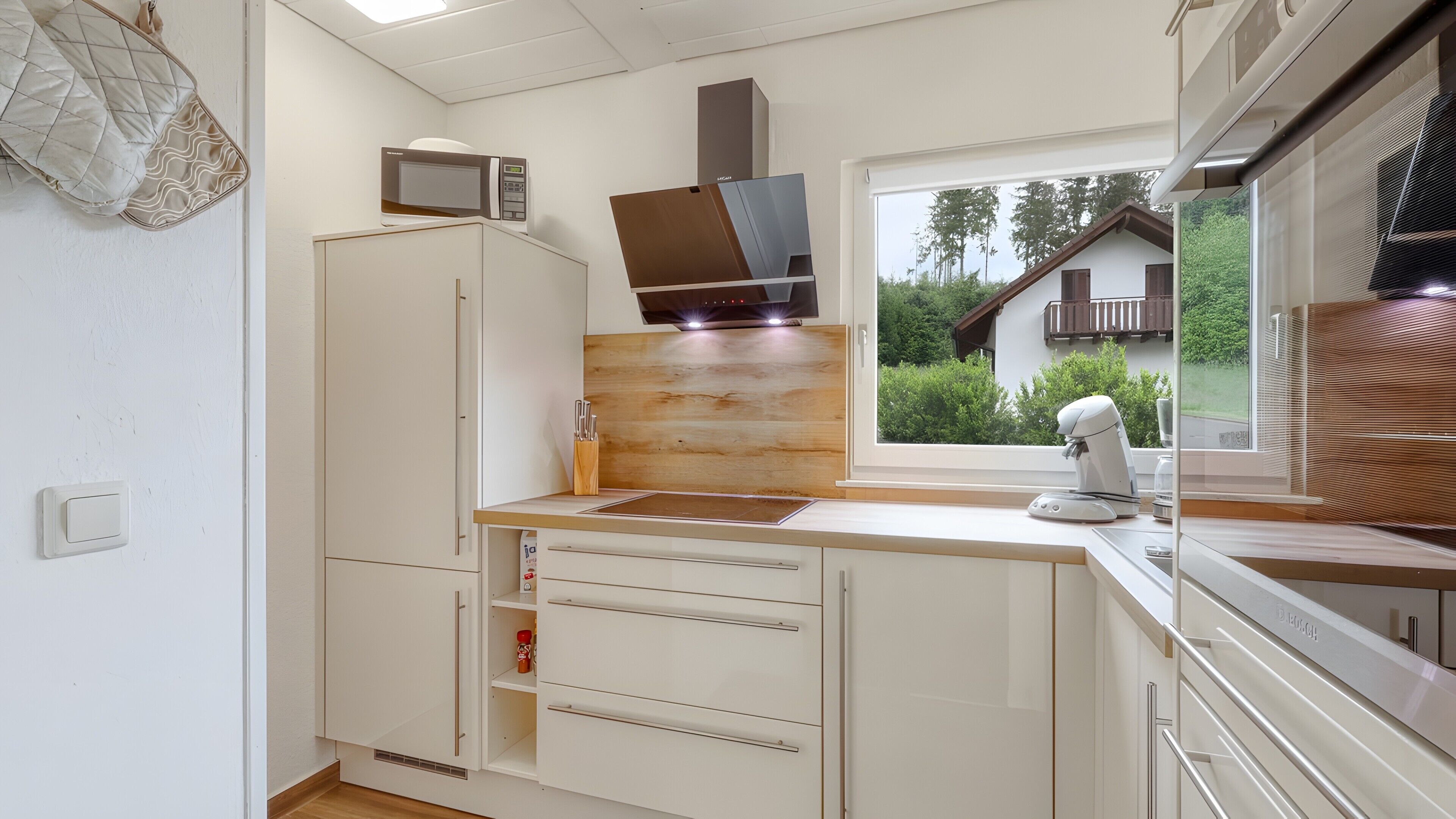 Eine Küche mit Mikrowelle, Backofen, Fenster mit Blick auf ein Haus und einer Kaffeemaschine.