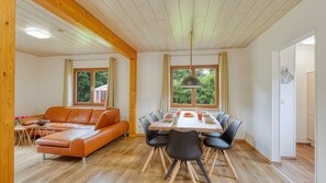 Un intérieur moderne avec un plafond en bois, une table à manger avec des chaises, un canapé et de grandes fenêtres avec des rideaux.