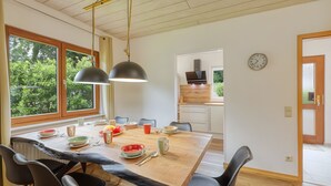 Un espace repas avec une table en bois, des chaises noires et des luminaires suspendus.