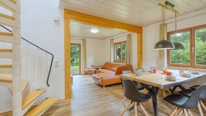 Un intérieur moderne avec un escalier en bois, un coin repas comprenant une table et des chaises, et un canapé en cuir.