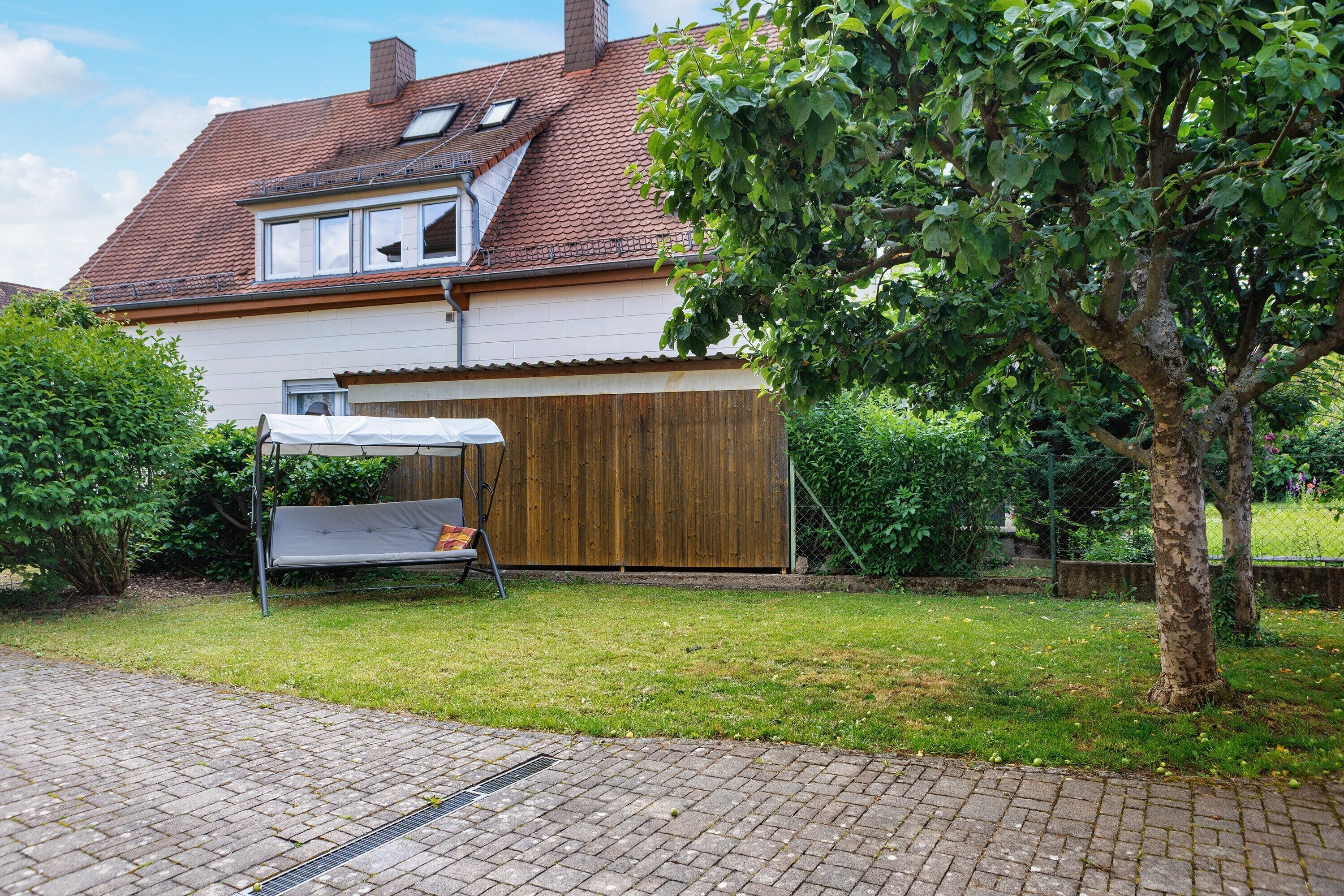 Une maison avec un toit en pente, un espace extérieur aménagé et couvert, et un arbre dans le jardin.